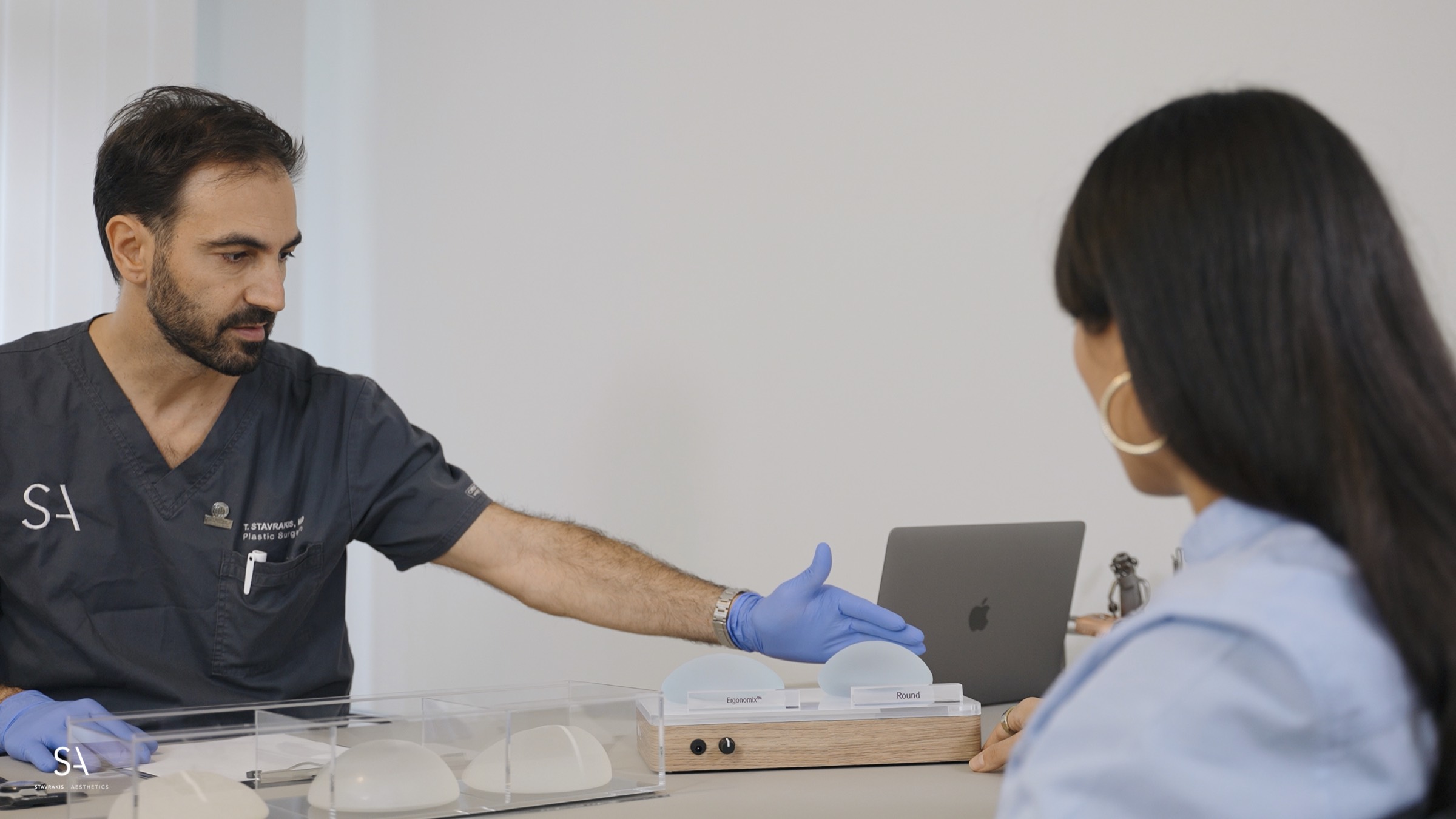 Dr. Stavrakis in consultation, handing a breast implant to a patient across the desk